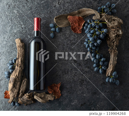 Bottle of red wine, blue grapes, and old vine snags on a black stone background. 119904268