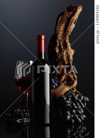 Bottle and glass of red wine with an old snag and blue grapes. 119904282