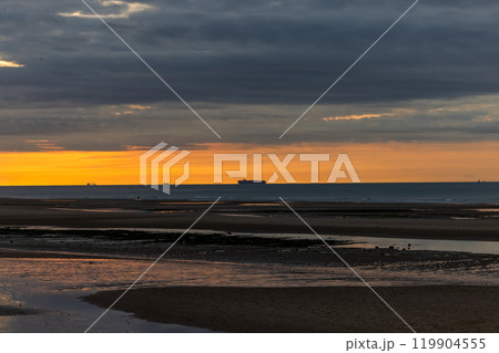 Dramatic sunset over calm sea, silhouetting cargo ship against tranquil beach backdrop Dramatic sunset over calm sea, silhouetting cargo ship against tranquil beach backdrop 119904555