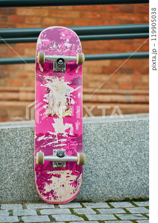 Used pink skateboard against stone wall in urban setting 119905038