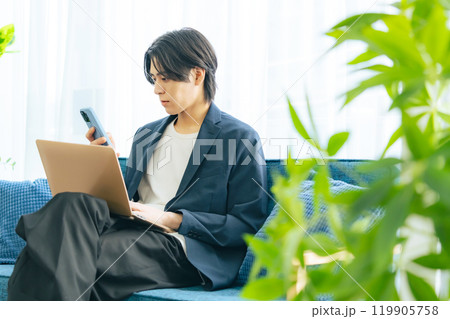 リビングでスマホとノートパソコンを使う男性 リビングでスマホとノートパソコンを使う男性 119905758