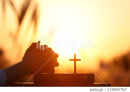 Christian praying with both hands together on the holy bible, autumn barley field sunset landscape, thanksgiving easter background Christian praying with both hands together on the holy bible, autumn barley field sunset landscape, thanksgiving easter background 119905767