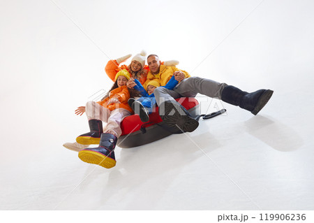 Happy family, mother, father and two kids, dressed in bright warm winter jackets, sliding in snow tube, having outdoor fun 119906236