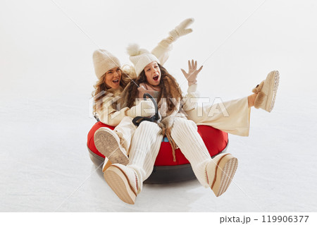 Joyful moment as mother and daughter laughing together while riding snow tube. Woman and girl dressed in cozy winter clothes Joyful moment as mother and daughter laughing together while riding snow tube. Woman and girl dressed in cozy winter clothes 119906377