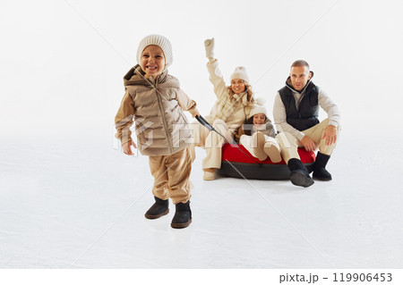 Happy family dressed in winter clothes enjoying time on snow, with little boy pulling tube. Winter outdoor fun and bonding. Happy family dressed in winter clothes enjoying time on snow, with little boy pulling tube. Winter outdoor fun and bonding. 119906453