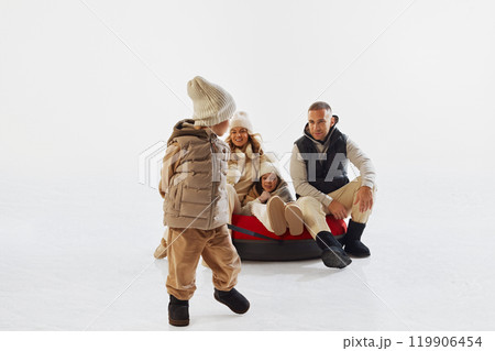 Happy family dressed in winter clothes enjoying time on snow, with little boy pulling tube. Winter outdoor fun and bonding. 119906454