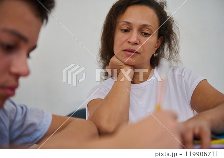 Mother closely helping her child with homework at home 119906711