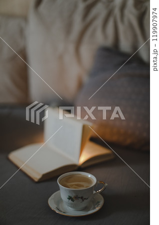 A cup of coffee and a book lying on the bed in a white bedroom 119907974