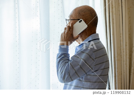 外を眺めながら電話をするシニア男性 外を眺めながら電話をするシニア男性 119908132