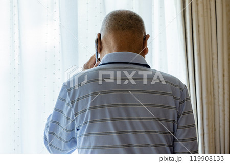 外を眺めながら電話をするシニア男性 外を眺めながら電話をするシニア男性 119908133