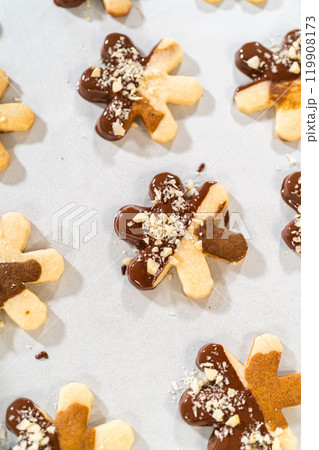 Creating cutout sugar cookies, partially dipped in chocolate and topped with hazelnut pieces, placed on parchment paper. Creating cutout sugar cookies, partially dipped in chocolate and topped with hazelnut pieces, placed on parchment paper. 119908173
