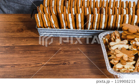 Crafting gingerbread cookie sandwiches with eggnog buttercream, presented on a rustic wooden table for Christmas gifting. Crafting gingerbread cookie sandwiches with eggnog buttercream, presented on a rustic wooden table for Christmas gifting. 119908215