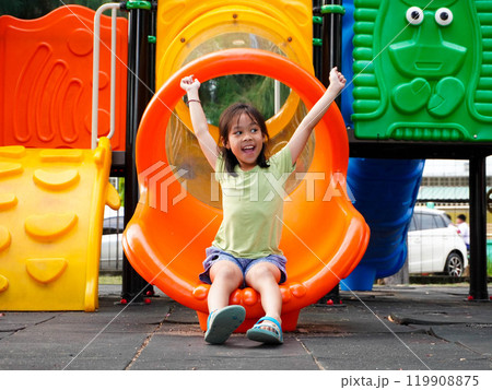 Children playing in the playground during summer vacation. Cute girl having fun on a colorful slide in an outdoor park. Children playing in the playground during summer vacation. Cute girl having fun on a colorful slide in an outdoor park. 119908875