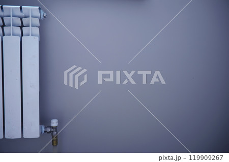 White modern aluminum radiator battery for hot water heating, on the background of a wall in the interior of an apartment or office space. White modern aluminum radiator battery for hot water heating, on the background of a wall in the interior of an apartment or office space. 119909267