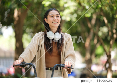 A woman wearing headphones and a brown jacket is riding a bike 119909851