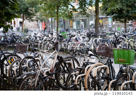 A crowded urban bicycle parking area showcasing eco-friendly transportation in a city. Represents sustainability, urban biking culture, and minimalist lifestyle trends with greenery in the background. A crowded urban bicycle parking area showcasing eco-friendly transportation in a city. Represents sustainability, urban biking culture, and minimalist lifestyle trends with greenery in the background. 119910143