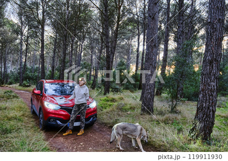 Car and adult woman lost in wooded area trying to orient herself at dusk. 119911930