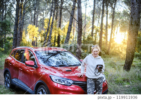 Woman taking pictures close to a car parked in a forest path. Woman taking pictures close to a car parked in a forest path. 119911936