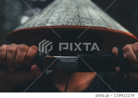 A determined samurai unsheathes his katana in a dark forest, representing honor and strength. Close-up of a courageous warrior slowly unsheathes his katana in front of his face. A determined samurai unsheathes his katana in a dark forest, representing honor and strength. Close-up of a courageous warrior slowly unsheathes his katana in front of his face. 119912239