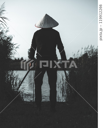 A samurai warrior wearing a traditional hat stands on the bank of a calm river at dusk holding katanas in his hands radiating an aura of strength and mystery. The samurai with the katana is thinking. A samurai warrior wearing a traditional hat stands on the bank of a calm river at dusk holding katanas in his hands radiating an aura of strength and mystery. The samurai with the katana is thinking. 119912266