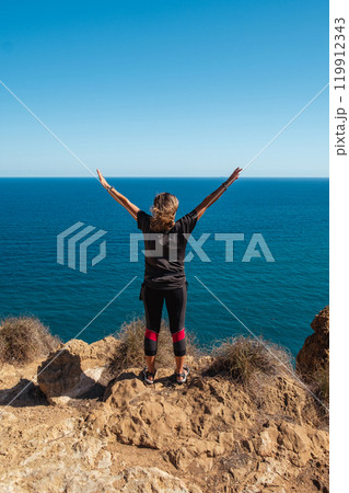 Girl standing on the edge of a cliff with outstretched arms Girl standing on the edge of a cliff with outstretched arms 119912343
