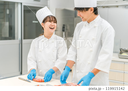 魚を調理するコックコート姿の男女スタッフ（調理師・セントラルキッチン・料理人・専門学校・食品加工） 119915142