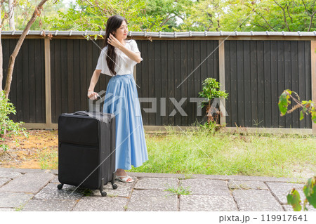 黒い塀の前の石畳の上をキャリーケースを引いて歩く若い女性旅行者 黒い塀の前の石畳の上をキャリーケースを引いて歩く若い女性旅行者 119917641