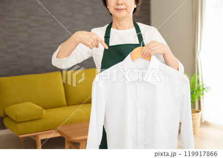 家のリビングでYシャツを指差す緑のエプロン姿のシニア女性主婦・家政婦 家のリビングでYシャツを指差す緑のエプロン姿のシニア女性主婦・家政婦 119917866