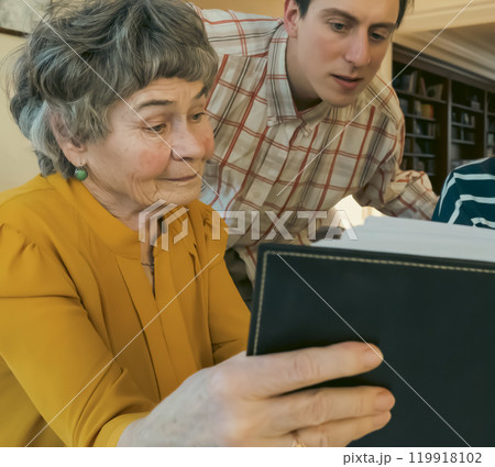 Family is looking photos at photo album together. Family is looking photos at photo album together. 119918102