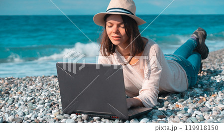 Girl in a hat works on a laptop on the beach, seashore. 119918150