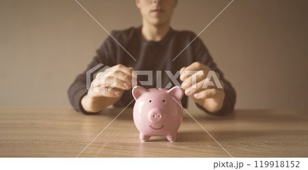 Young man with a piggy pank, takes care about his savings 119918152
