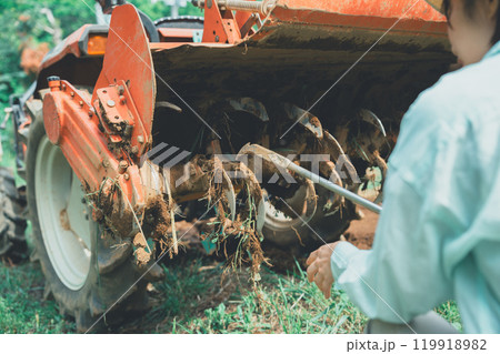 トラクターロータリーの泥落としをする女性 119918982