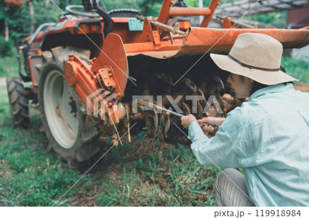 トラクターロータリーの泥落としをする若い女性 119918984