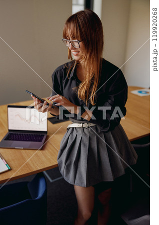 A professional woman actively engaged with her smartphone in a contemporary office environment A professional woman actively engaged with her smartphone in a contemporary office environment 119920268