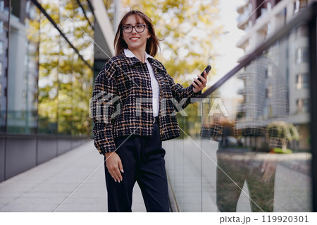 A Stylish Young Woman Holding a Phone in a Vibrant Urban Setting Filled with Life A Stylish Young Woman Holding a Phone in a Vibrant Urban Setting Filled with Life 119920301