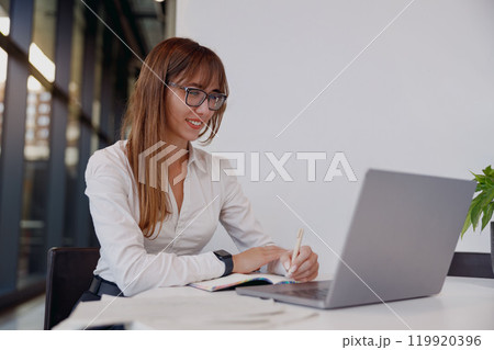 A Young Businesswoman Engaged in Work on Her Laptop While Seated in a Modern Office Environment 119920396
