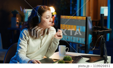 Photo editor editing images lighting and color balance, delivering visually appealing final product, listening to music. Freelancer wearing headphones, browsing through photographs, camera A Photo editor editing images lighting and color balance, delivering visually appealing final product, listening to music. Freelancer wearing headphones, browsing through photographs, camera A 119920851