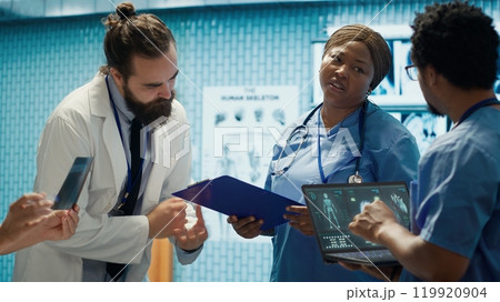 Medical professionals review x ray results and discuss patient care strategies during a meeting. Team of licensed healthcare experts working to provide accurate diagnosis in a clinic. Camera A. 119920904