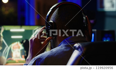 Man having fun playing videogames on PC while chatting with teammates. Excited gamer battling rival players, communicating with friends through headset microphone, camera A 119920956