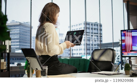 Woman CEO reviewing sales reports and market trends from analytics files, using data driven insights to adjust strategies and maximize business growth opportunities. Strategic thinking. Camera B. 119920986