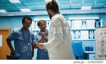 Cheerful confident doctors and nurses finding right treatment plan for a diagnosis, competent healthcare industry workers. Medical staff smiling and clapping hands, good news in a cabinet. Camera B. 119920997