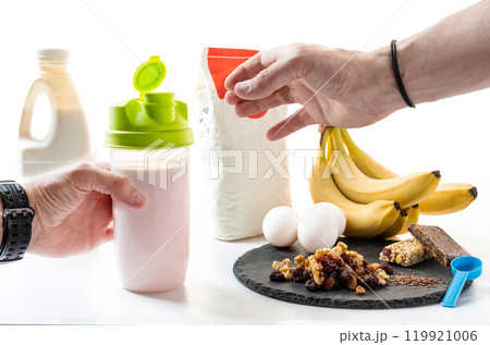 Shaker in hands. Making a milkshake. Cocktail with bananas and dried fruits. Sports cocktail. Sports food. Isolated. Shaker in hands. Making a milkshake. Cocktail with bananas and dried fruits. Sports cocktail. Sports food. Isolated. 119921006