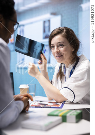 Physician presenting x ray imaging for the right diagnostic during check up, explaining the lab test results and treatment at medical consultation. Medic showing examination results in cabinet. 119921073