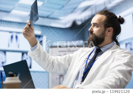 Licensed physician working on finding the right diagnostic with x ray scans results, examining bones radiography to detect illness. Medic analyzing healthcare records in hospital cabinet. 119921120