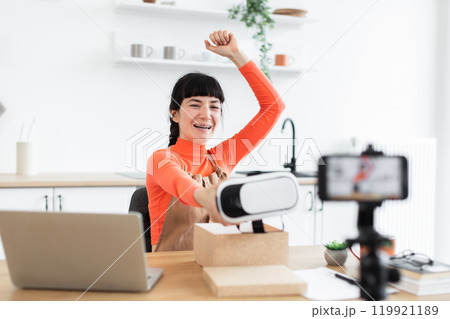 Caucasian female blogger excitedly unboxing virtual reality headset on camera 119921189