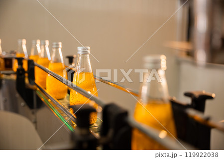 Transparent bottles move along the conveyor belt in the beverage factory filled with organic basil or chia seed drinks blended with pomegranate. Automated clean technology ensures quality liquid. 119922038