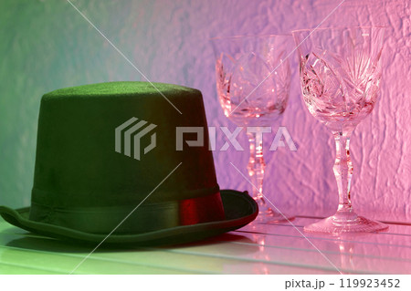 Black hat, shining crystal wine glasses on pink light Black hat, shining crystal wine glasses on pink light 119923452