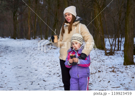 Snack in nature.Mother with baby girl eat and drink in winter park Snack in nature.Mother with baby girl eat and drink in winter park 119923459