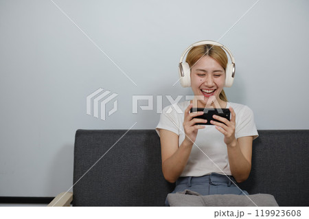 A woman is sitting on a couch and playing a video game on her phone 119923608