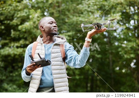 Waist up portrait of smiling African American man holding drone while enjoying nature videography in green forest copy space 119924941